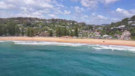 Aerial-toward-surfers-and-the-beach-buildings-and-homes-on-the-cliffs-beyond
