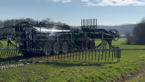 Un-Tractor-De-Maquinaria-Agrícola-Grande-Esparció-Lodo-En-El-Campo-Agrícola-De-Pasto-En-Primavera