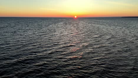 Colorful-sunset-over-a-vast-ocean,-with-a-small-boat-silhouetted-against-the-vibrant-sky-Atlantic-Ocean-at-sunset,-possibly-near-the-coast-of-New-Jersey-Delaware,-in-the-United-States