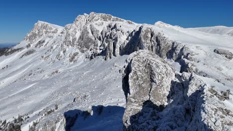 Snow-covered-Strungile-Mari-Peak-under-a-clear-blue-sky,-Bucegi-Mountains