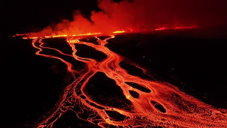 Fissure-volcanic-eruption-exploding-at-night-with-glowing-lava-in-Iceland,-aerial