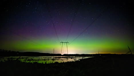 Timelapse-of-Aurorae-and-clouds-above-electric-wires-and-wet,-mirroring-fields