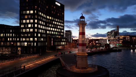 Antiguo-Faro-De-Malmo-Frente-Al-Mar-Con-Edificios-Iluminados,-Antena-Nocturna