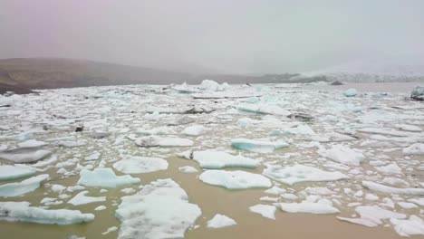 Flyover-a-glacier-lagoon-filled-with-floating-icebergs-on-a-foggy-day-in-Iceland