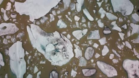 Von-Oben-Nach-Unten-überfliegen-Von-Eisbergen,-Die-In-Einer-Braunen,-Schlammigen-Gletscherlagune-In-Island-Schwimmen