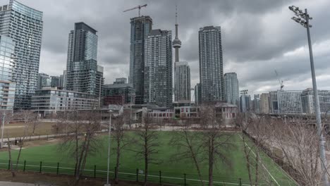 Children-play-on-sports-field-by-skyscrapers-in-cloudy-Toronto,-timelapse