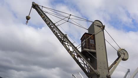 Panning-clip-looking-up-at-large-metal-crane-with-blue-sky-background,-at-old-Genoa-Port,-Porto-Antico,-Italy