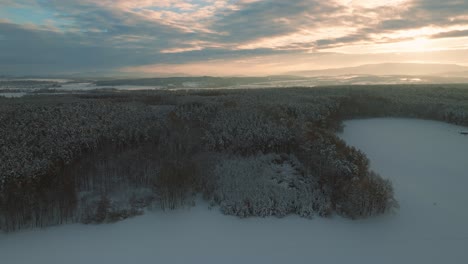 Aerial-drone-flight-over-snow-covered-forest-in-winter,-cold-weather,-peaceful-relaxing-view-during-sunset-or-sunrise