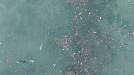 Von-Oben-Nach-Unten-Aufsteigende-Drohnenaufnahme-Von-Verschmutztem-Wasser-Voller-Plastikmüll-Und-Abgestorbenem-Korallenriff-Im-Türkisfarbenen-Tropischen-Wasser-Des-Balangan-Beach-In-Uluwatu,-Bali,-Indonesien
