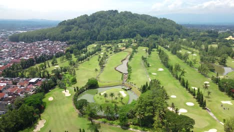 Aerial-view-of-golf-course-in-the-middle-of-Magelang-City-with-small-hill-on-the-background