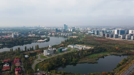 Vista-Aérea-De-Los-Suburbios-De-Bucarest-Con-Lago,-Follaje-Otoñal-Y-Edificios-Modernos