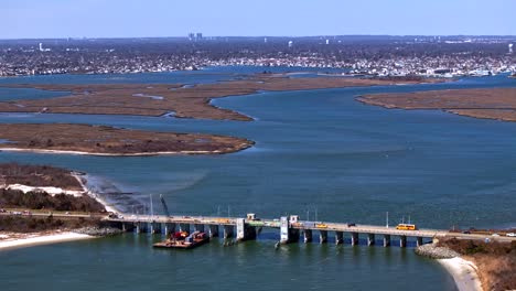 Un-Lapso-De-Tiempo-Aéreo-Sobre-Un-Arroyo-En-Long-Island,-Nueva-York,-Con-Un-Puente-Para-Vehículos-En-Reparación-En-Un-Día-Soleado