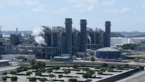 Behold-massive-clean-energy-natural-gas-plant-with-billowing-white-smoke,-set-against-the-USA-Flag-waving-in-the-video-background,-representing-sustainable-energy-practices-and-patriotism