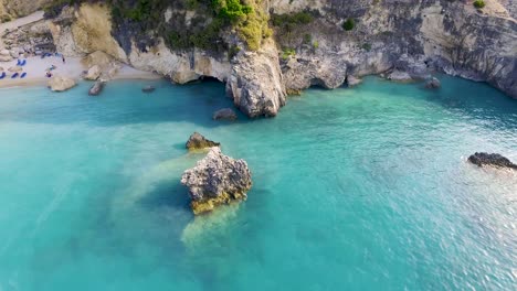 Orbiting-drone-shot-above-the-crystal-clear,-blue-waters-of-the-Ionian-Sea-in-front-of-the-rugged-cliffs-of-Xigia-Beach-in-Zakynthos-Island-in-Greece