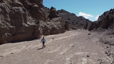 Camera-rotates-to-follow-woman-walking-alone-in-rugged-narrow-canyon