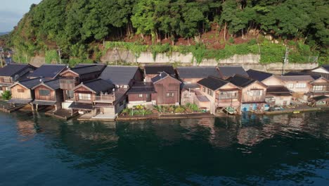 boat-houses-establishing-shot-in-Kyotango-Japan-seaside-village-home-valley-green-hills-mountain-background,-Drone-Aerial-view-ine-town-inecho