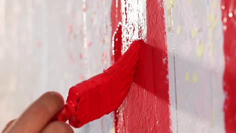 A-man-is-painting-a-wall-in-red-color-with-brush,-close-up-shot,-insert-shot