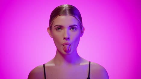 Naughty-young-woman-sticks-out-tongue,-looking-at-camera,-studio-shot,-purple