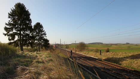 Red-Deutsche-Bahn-freight-train-moving-through-rural-landscape-on-sunny-day,-clear-sky-in-background