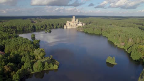 Aerial-wide-dolly-shot-of-the-Castle-of-Stobnica,-Poland---a-big-tourist-attraction-built-on-an-artificial-island-on-a-lake-in-the-middle-of-an-unhabituated-forest