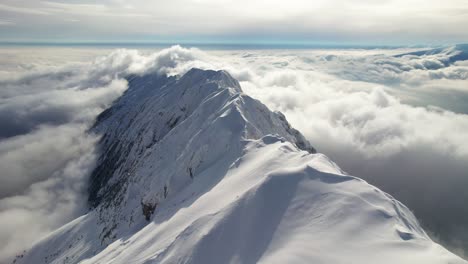 Snow-capped-Piatra-Craiului-Mountains-peaking-through-a-sea-of-clouds-under-a-blue-sky,-aerial-view