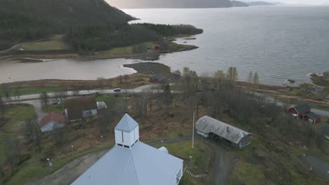 Eine-Weiße-Kirche-In-Sorreisa,-Norwegen,-In-Der-Nähe-Eines-Fjords-Mit-Bewölktem-Himmel,-Luftaufnahme