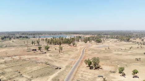 Wide-aerial-shot-of-barren-arid-land-with-asphalt-road-and-water-at-a-distance-in-Charu-village-in-Chatra,-Jharkhand,-India