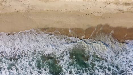 Luftaufnahme-Von-Oben-Nach-Unten-Von-Wellen,-Die-Bei-Sonnenuntergang-Am-Sandstrand-Entlang-Des-Pazifischen-Ozeans-Brechen