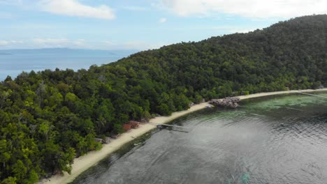 Reveal-shot-of-guest-houses-along-sandy-beach-in-front-of-thickly-overgrown-island-landscape