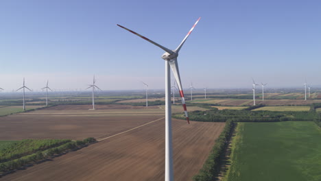 Profile-aerial-of-a-static-Wind-Turbine-surrounded-by-rotating-turbines-in-a-flat-farmland-environment-in-Monchhof,-Austria