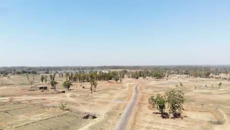 Aerial-shot-of-barren-arid-land-with-asphalt-road-and-water-at-a-distance-in-Charu-village-in-Chatra,-Jharkhand,-India