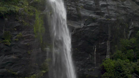 Slow-Motion-pan-down-a-small-waterfall-on-a-cliff---Milford-Sound-,-New-Zealand
