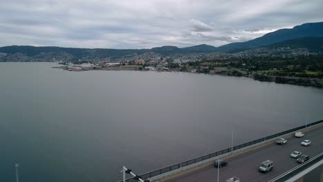 Backward-drone-view-of-city-with-bridge-under-a-cloudy-sky