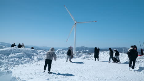 People-walking-below-wind-turbine-at-snowy-Daegwallyeong-Sky-Ranch,-Korea