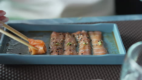A-woman-with-chopsticks-in-hand-takes-thin-slices-of-salmon-marinated-with-sesame,-herbs-and-sauce