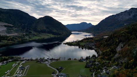 Austrian-Alps-Grundlsee-Crystal-clear-lake-surrounded-by-lush-green-trees-and-mountains-under-a-clear-blue-sky-with-a-few-white-clouds,-captured-from-an-aerial-viewpoint