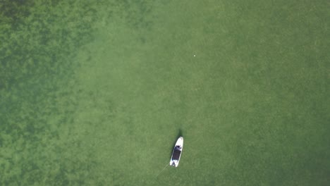 A-lone-boat-floating-on-the-clear-waters-of-los-roques-during-daylight,-aerial-view