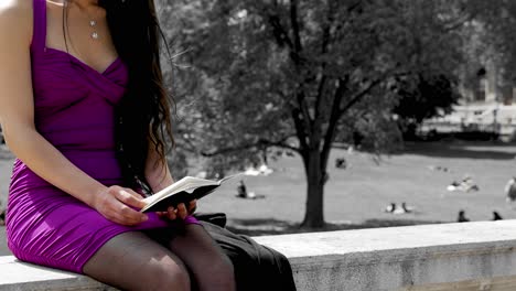 Pretty-girl-reading-in-notebook-in-front-of-park,-education-setting,-university