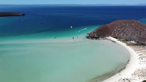 Drone-view-of-Playa-Balandra-in-La-Paz,-Mexico-with-yachts,-sailboats,-and-slow-motion