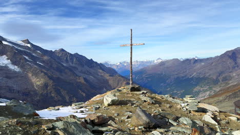 Taschhorn-mountain-top-Christian-Catholic-Jesus-Christ-Cross-on-rocky-snowy-peak-Saas-Fee-Saastal-Zermatt-Switzerland-Swiss-Alps-religious-peaceful-blue-sky-high-clouds-slow-pan-to-the-left