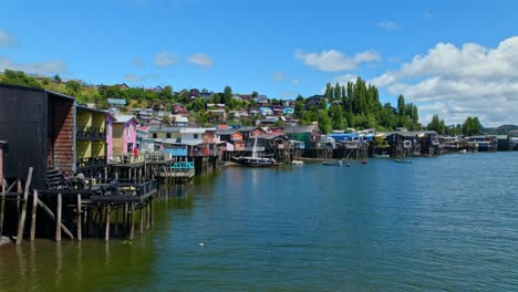Drone-flying-toward-a-ship-in-front-of-the-Palafitos-stilt-houses-of-Castro,-Chile