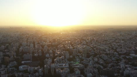 Vista-Aérea-De-Drones-En-La-Hora-Dorada,-Donde-Hay-Muchos-Edificios-De-Gran-Altura-Y-Edificios-De-Poca-Altura-Brillan-Y-También-Se-Ven-Casas-Residenciales-Y-También-Hay-Un-Gran-Templo