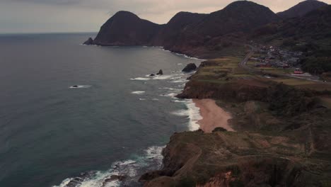 Japan-Kyotango-Aerial-drone-panoramic-fly-above-cliff-and-beach-shoreline-sunset-pink-skyline,-establishing-shot-of-mountains-islands-and-natural-environment-Japanese-Summer