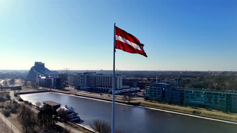 A-red-and-white,-Latvia-flag-is-flying-high-above-a-city-Riga