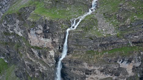 Waterfall-cascading-down-rugged-cliffs-with-a-view-of-Lago-Niera,-serene-nature-scenery