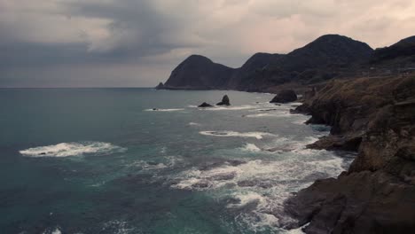 Aerial-Panoramic-Close-up-drone-above-Blue-Japanese-sea-in-Kyoto-Kyotango-Beach-Cliff,-summer-white-sand-coastline-with-hills-and-rock-islets