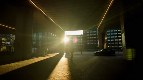 Hombre-Caminando-Bajo-El-Paso-Elevado-Urbano-Con-Sol-Cálido-Y-Bajo-Como-Luz-De-Fondo-En-Un-Suburbio-Moderno