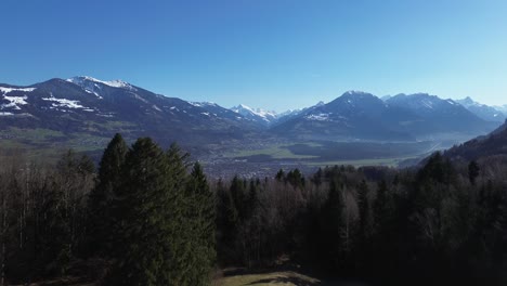 Drone-Levanta-Una-Toma-De-Campo-Verde-Con-Pequeñas-Cabañas-En-Primer-Plano-Y-Paisaje-Urbano-Y-Montañas-Nevadas-En-El-Fondo,-Vista-Aérea-Sobre-Nenzing-Austria