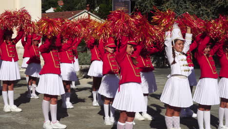 Lindas-Chicas-Majorette-Con-Uniformes-Rojos-Actuando-Con-Pompones-En-La-Plaza-De-La-Ciudad