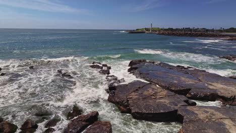 The-splash-of-surf-over-wet-rocks-with-two-light-houses-and-Wollongong-Harbour-beyond